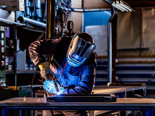 The welder performs welding task at his workplace in the factory, while the sparks "fly" around, he wears a protective helmet.